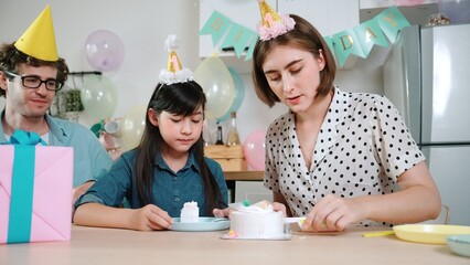 Caucasian mother cutting cake while family congratulate in girl's birthday. Diverse family...