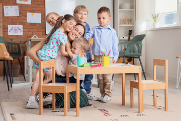 Little children hugging nursery teacher during art lesson in kindergarten
