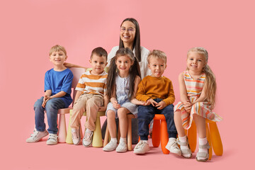 Little children with nursery teacher sitting on pink background