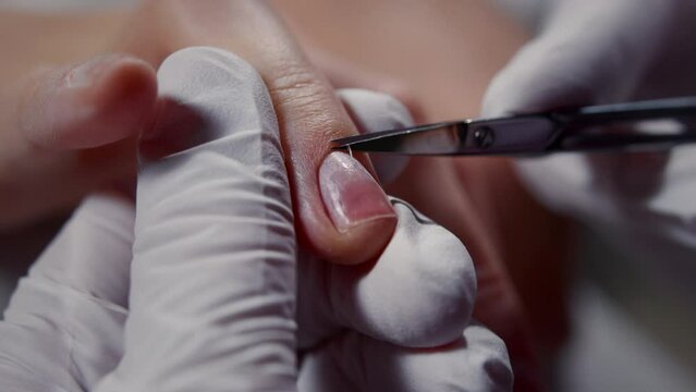 A manicure master uses cuticles to trim the nails of a client in a beauty salon. The nail art master uses scissors to cut off parts of the skin on women's hands. Cuticle removal from a finger close-up
