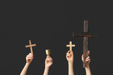 Female hands with wooden crosses and cup on dark background. Good Friday concept