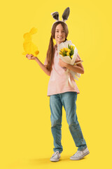 Cute little girl with Easter bunny ears, decor and flowers on yellow background
