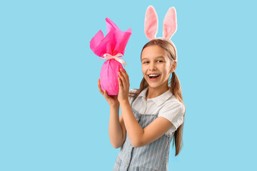 Cute little girl with Easter bunny ears and gift on blue background