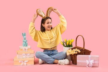 Cute little girl with Easter bunny ears, flowers and gifts on pink background