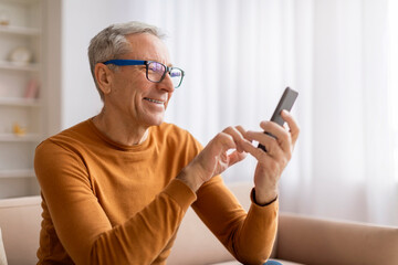 Grandfather wearing eyeglasses using cell phone at home