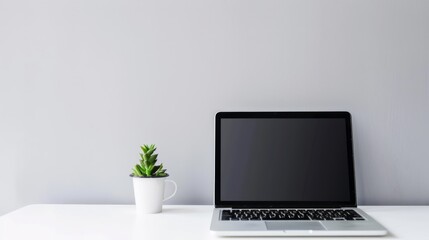 Minimalistic white background of office table with white laptop, coffee and plant on it. Shows the working environment.