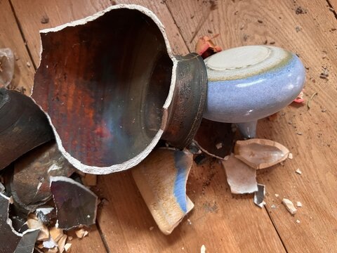 Close up of broken ceramic art and antique china vase, vintage bowl contain lavender and plates shapes and colour pieces destroyed by fall from collapsed mantelpiece to oak wood floor in old house