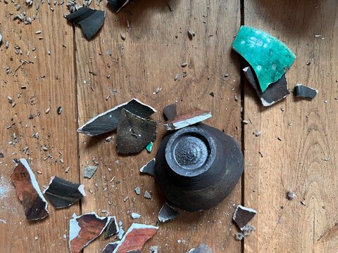 Close up of broken ceramic art and antique china vase, vintage bowl contain lavender and plates shapes and colour pieces destroyed by fall from collapsed mantelpiece to oak wood floor in old house