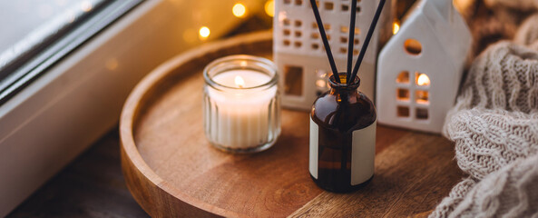 Fototapeta na wymiar Banner. Cozy home decor, hygge and aromatherapy concept. Aroma diffuser, burning candle, Christmas perfume on wooden bamboo tray, knitted sweater. Comfortable atmosphere, Scandinavian decor.