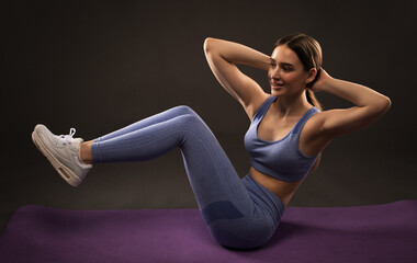 Obraz premium A slender female bodybuilder in a lilac tracksuit does an exercise to burn belly fat and does cardio. Sports concept, fat burning and healthy lifestyle.