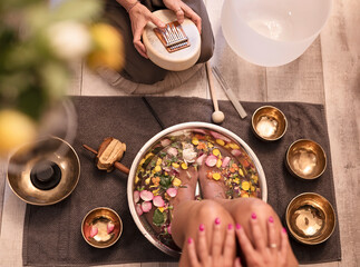 Female feet at spa salon with sound healing. Legs of woman in bowl with flowers and petals of rose....
