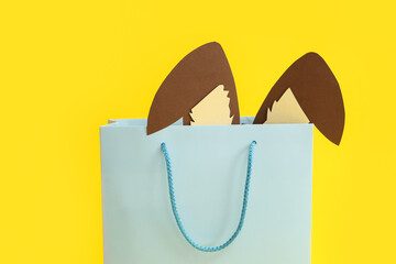 Shopping bag with paper Easter bunny ears on yellow background