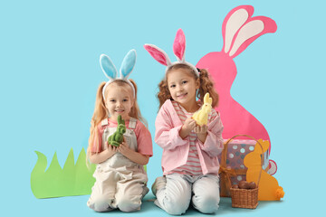 Cute little girls in bunny ears with Easter rabbits, eggs and paper decor on blue background