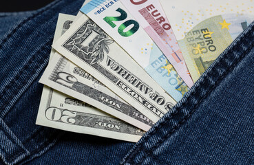 Banknotes of different denominations of euro and US dollar in a jeans pocket close-up.