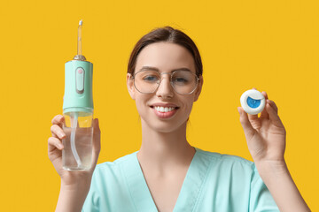 Female dentist with oral irrigator and dental floss on yellow background