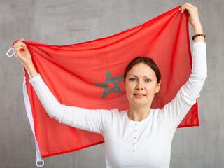 Smiling relaxed adult female tourist waving national flag of Morocco while looking at camera at...