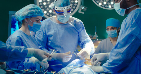 Professional surgeon sutures patient in operating room. Group of medical workers wearing special...