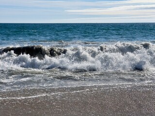 Fototapeta na wymiar Pacific Ocean waves foaming as they break on sandy beach in Southern California, bright sunny day