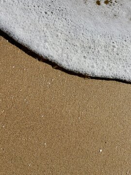 Sea foam washes in as ocean wave breaks on a sandy shore. Daylight, detail, creating abstract image for potential use as graphic background
