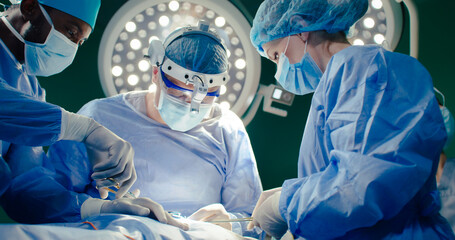 Remote shoot. Three medical workers in operating room. Chief doctor in binoculars. African American...