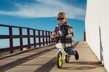 Cute little boy rides a jogging bike down the road on a sunny day, the child plays and rides his bike.