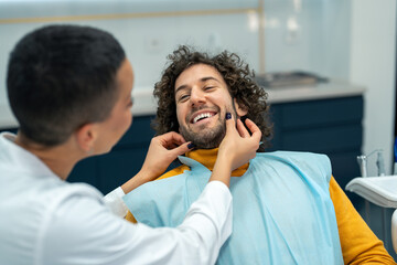 Smiling man at dentist appointment. Happy man with curly hair during teeth check-up at dental...