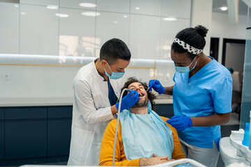Two female dental specialists and male patient during dental procedure at dental clinic. Man is...