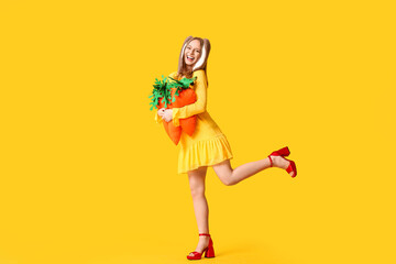 Happy woman in bunny ears with toy carrots on yellow background. Easter celebration