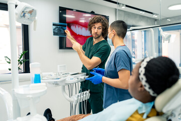 Male dentist in a dental office talking with a female colleague while showing a x-ray image of a...