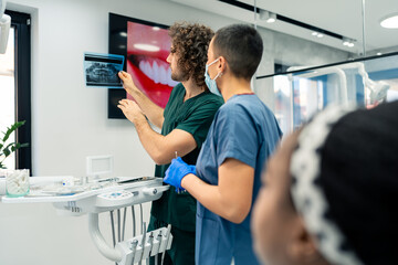 Two interracial dentists discussing a dental x-ray image before starting a treatment.