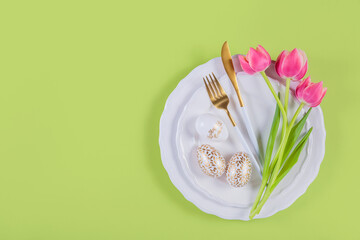 Pink tulips, table place setting and festive easter decor on green background