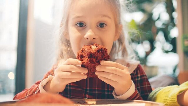 Beautiful blonde little girl eats muffin in a cafe