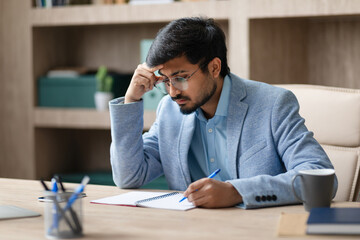 Indian entrepreneur man taking notes with concerned expression in office