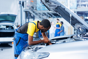 Repairman in car service uses torque wrench to tighten bolts after replacing battery. Certified...