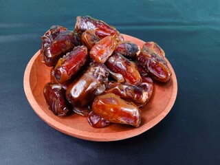 Close up of a pile of dates served on a wooden plate on a black background. sweet brown fruit. healthy meals. food for breaking the fast