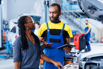 Mechanic at auto repair shop conducts annual vehicle checkup, informing customer about needed motor oil replacement. BIPOC garage worker talks with customer after finishing car inspection