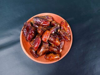 Top view of a pile of dates served on a wooden plate on a black background. sweet brown fruit. healthy meals. food for breaking the fast