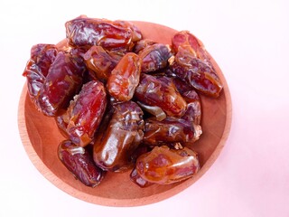 Close up of dates isolated on pink background. a pile of dates served on a wooden plate on a pink background. sweet brown fruit. healthy meals. food for breaking the fast