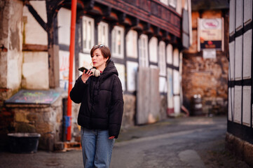 Engrossed in communication, a woman records a voice memo on her phone, surrounded by the rustic charm of an old city alley
