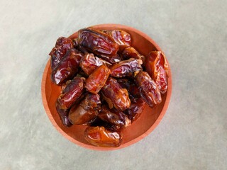 a pile of dates served on a wooden plate on a gray background. sweet brown fruit. healthy meals. food for breaking the fast. Top view