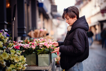 In an urban flower market, a woman in a black jacket is fully engaged in selecting the perfect...