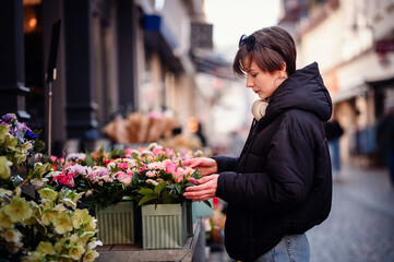 In an urban flower market, a woman in a black jacket is fully engaged in selecting the perfect...