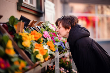 A woman leans in to savor the fragrance of bright, fresh flowers at an outdoor market, creating a...