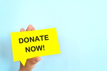 Human hand holding speech bubble with written phrase Donate Now. Charity donations call invitation.