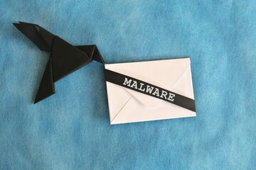 Black raven paper origami carrying white letter envelope with word Malware. Receiving malware...