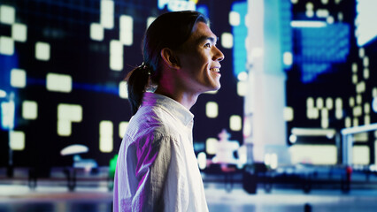Asian man wandering around city streets at night, looking upwards to surrounding condominiums in...