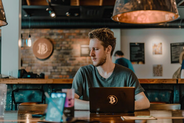 Entrepreneur working on cryptocurrency strategies in a café with a Bitcoin sticker on his laptop