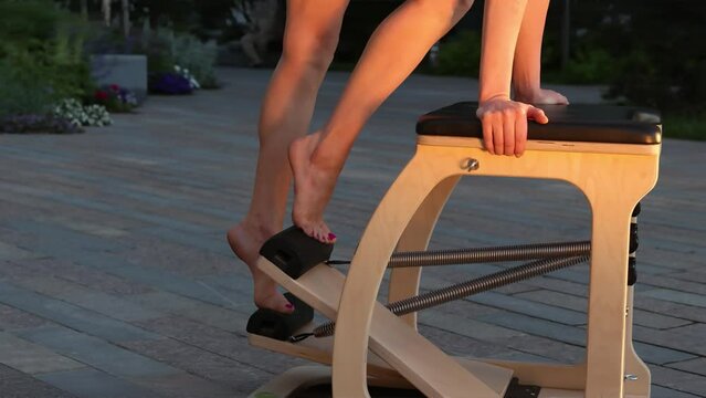 Working on footwork on a reformer pilates chair. Close-up of a female athlete's feet. Effective pilates training in modern studio blonde woman stretching back and leg muscles on reformer 
