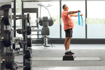 Mature man in sportswear exercising with a stretch strap on a step aerobic platform at the gym