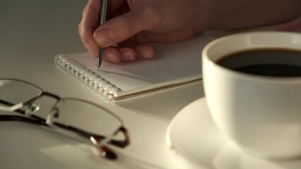 Closeup of woman's hands journaling in a white notebook on a white table at home.